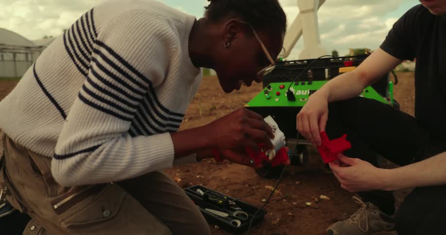 A man and a woman are fiddling with a red object outdoors with a green object behind