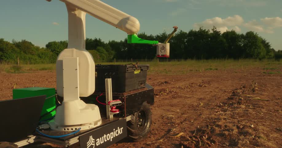 A robotic farming vehicle is operating in a rural field under a partly cloudy sky