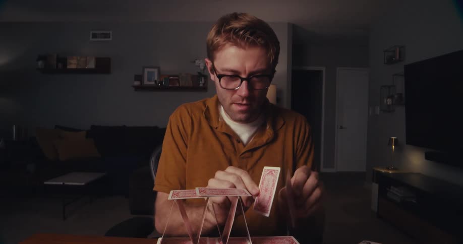 Timelapse of a man building a pyramid out of playing cards in a living room