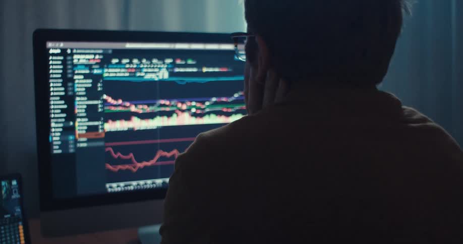 Man stares at monitor full of charts while holding head in hands