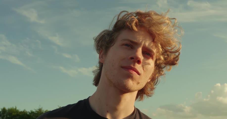 A young teenager stands in the open on a sunny day as the wind gently blows his hair