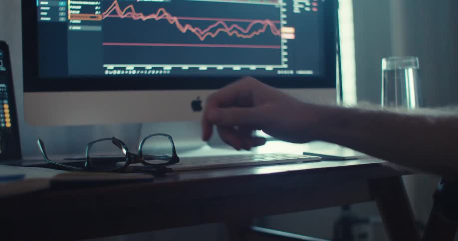 A person sitting in front of a computer puts their glasses on the desk and starts drumming their fingers