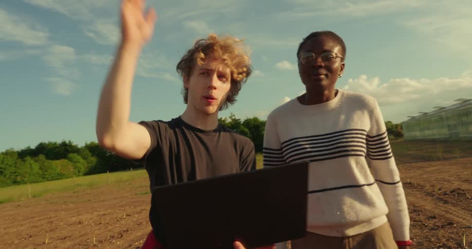 A man and woman look at a computer screen while standing in a farm field