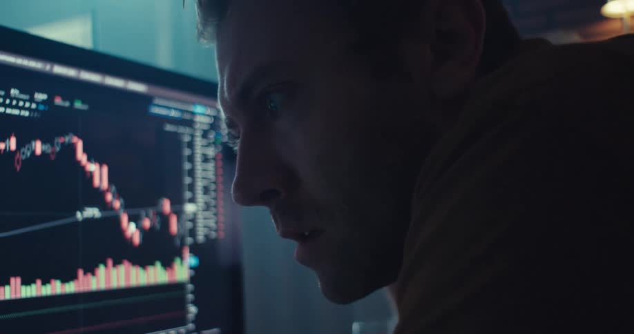 A man watches the stock market chart on a monitor and computer screen with serious focus