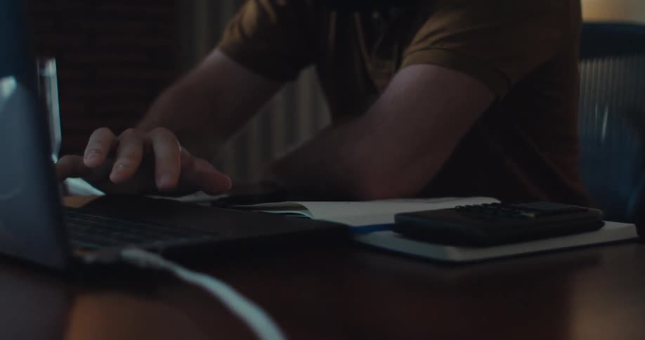 A man sits at a desk while tapping the trackpad of a laptop and staring at the screen