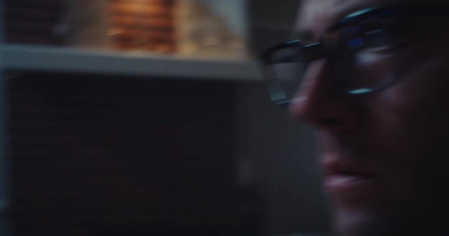 A man wearing glasses watching the stock market chart on his computer screen indoors
