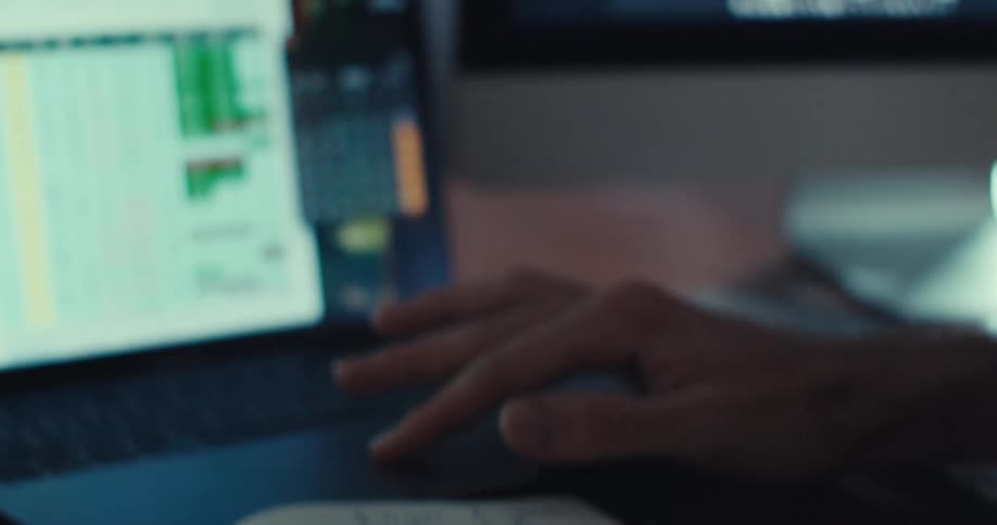 A man sitting using a laptop and reading a notebook with some notes