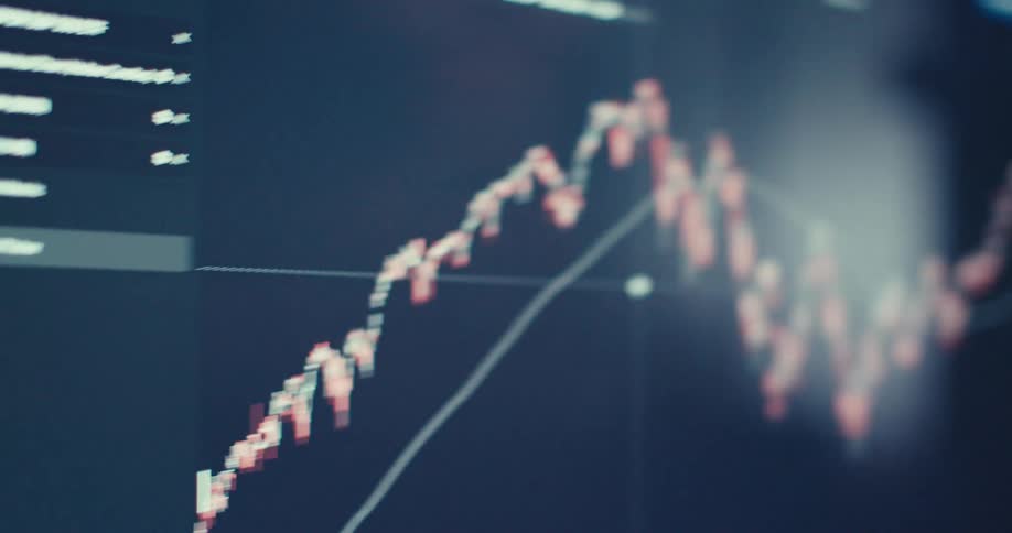 A man intently looks at a computer screen displaying a fluctuating stock chart
