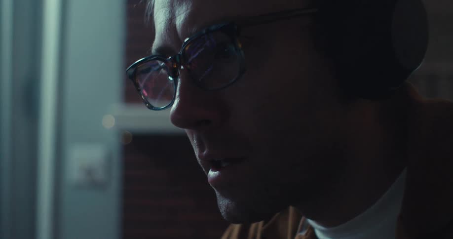 Man talks and leans forward to concentrate on his computer while the display is reflected in his glasses