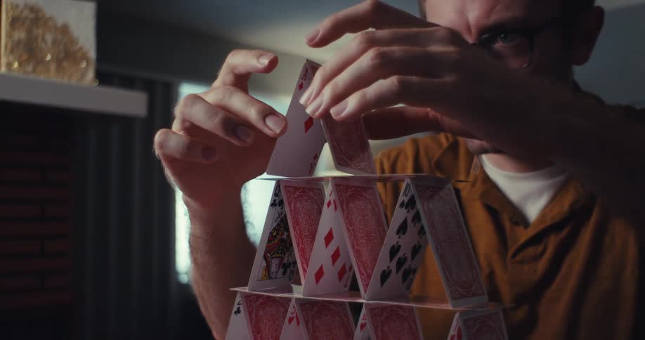 A man wearing glasses building a house of cards in his living room