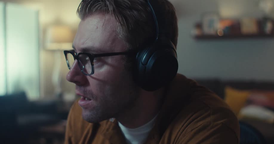 A man wearing a headset looks at a computer screen expressing a confident achievement