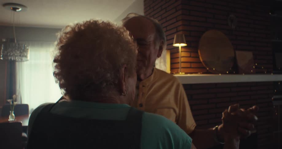 An elderly couple happily dancing in a living room at home
