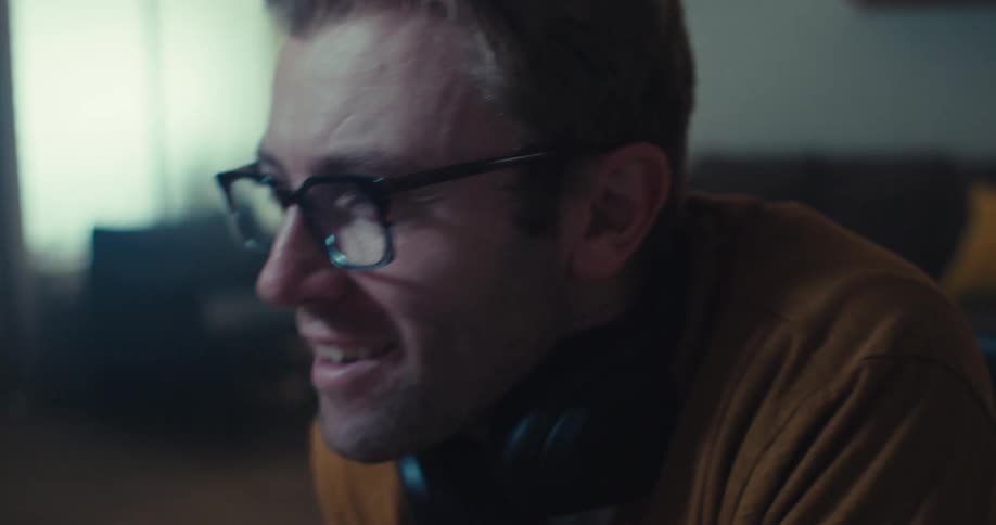 A man is sitting in a living room looking intensely at something and smiling
