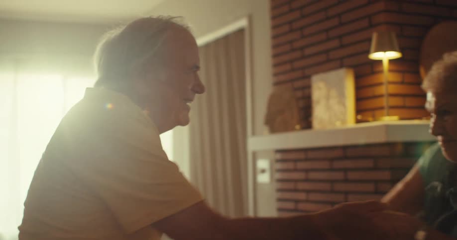 A closeup of a joyful elderly couple dancing in their sunlit living room