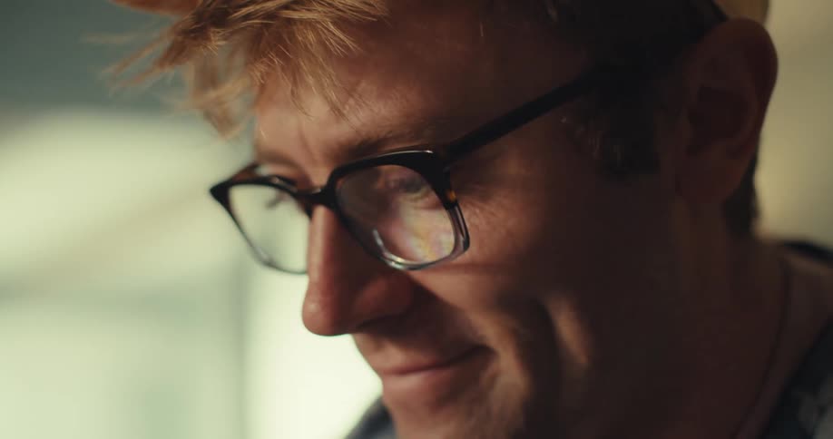 A man wearing glasses picks up a puzzle cube and tries to solve it