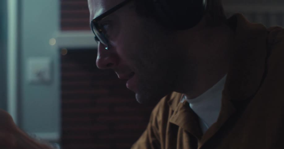A man wearing headphones and eyeglasses is talking on the computer