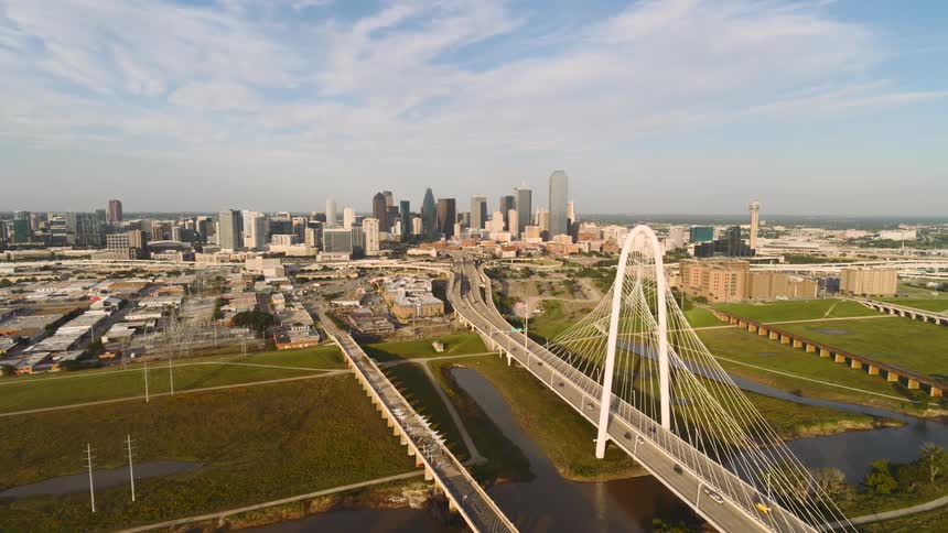 A wide aerial shot of a suspension bridge leading into the dallas city skyline on a clear day