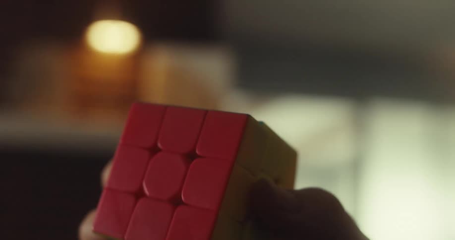 A man smiles as he holds and spins a solved rubiks cube in his hands