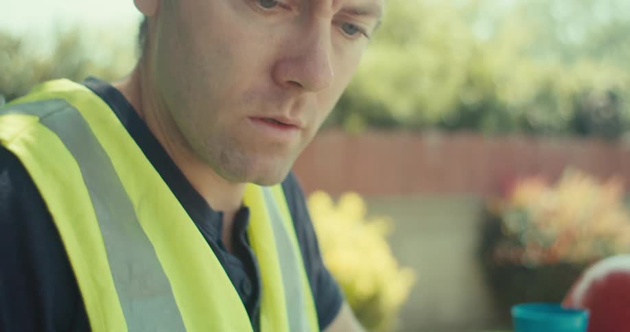 A construction worker types on his cell phone while looking at blueprints