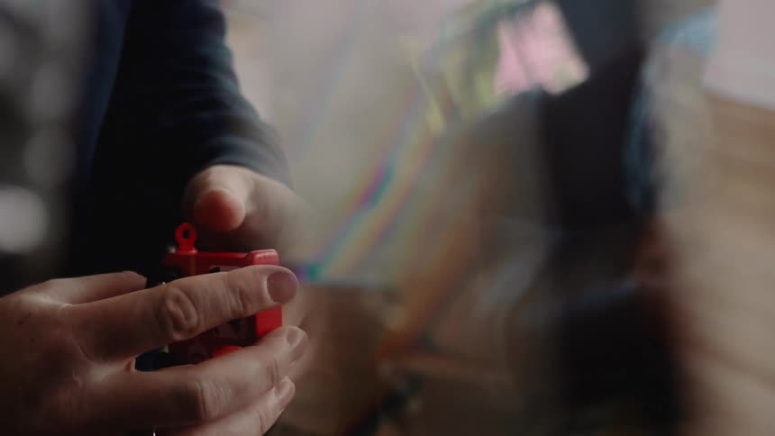 A persons hands hold a small red toy train with black accents viewed through distorted glass