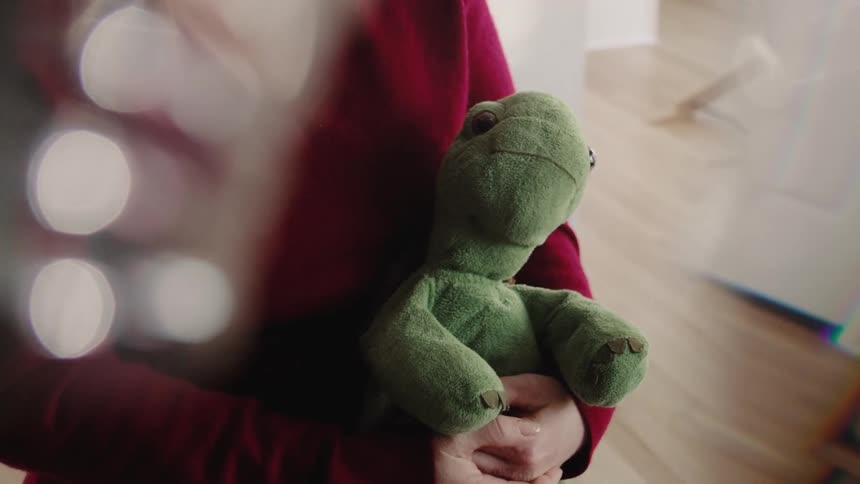 Woman stands indoors holding a stuffed toy