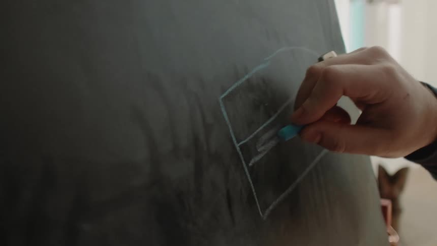 A person draws a rectangle on a chalkboard using blue chalk in a welllit room