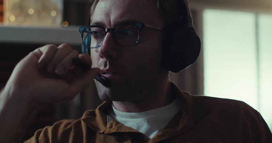 A man sitting in a room listening through his headphones and gesturing