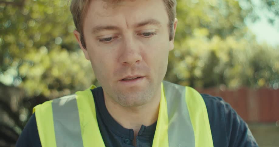 A man is sitting outside looking at blueprints and writing on notes