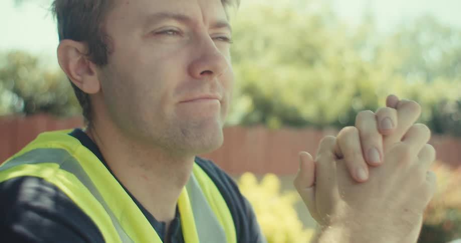 A man in a safety vest sits at a table with blueprints sticky notes a hard hat and a cup outdoors