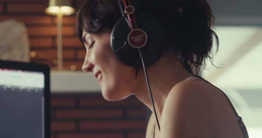 Woman dances as she happily creates beats with electronic equipment in a room