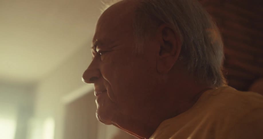 An elderly man dances alone indoors warmly lit by natural sunlight