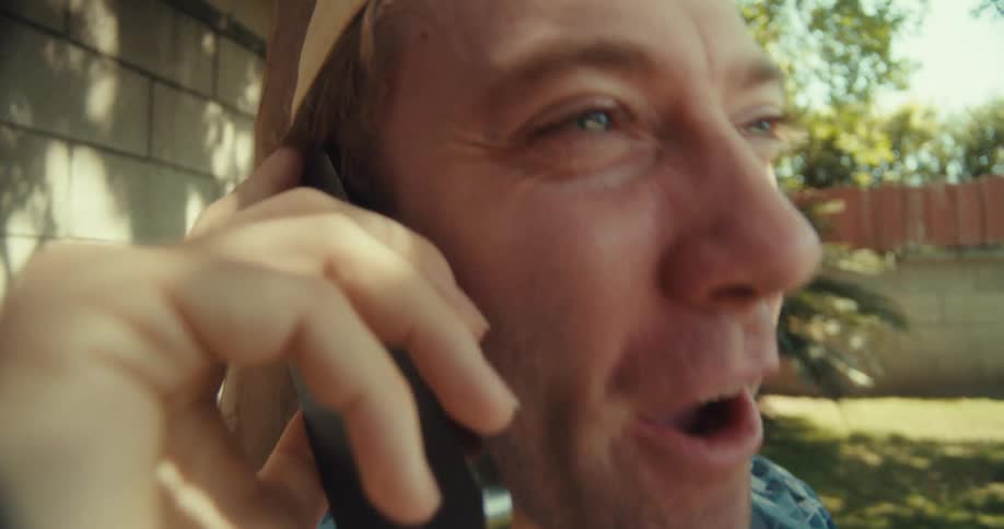Man sitting on a blanket in the backyard comically talking on a cell phone