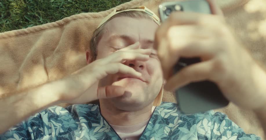 A man is laying on a blanket on the grass while on a video call