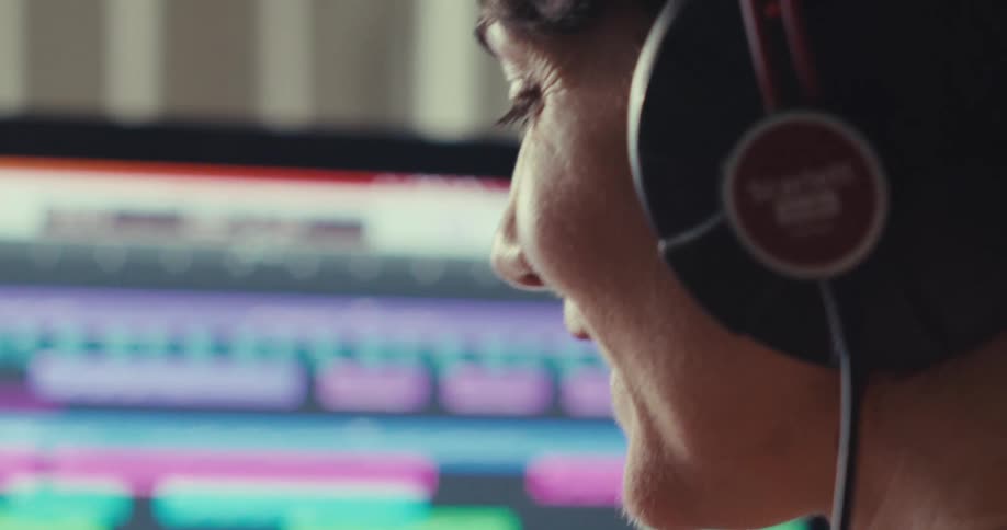 A person with headphones monitors a colorful audio workstation screen