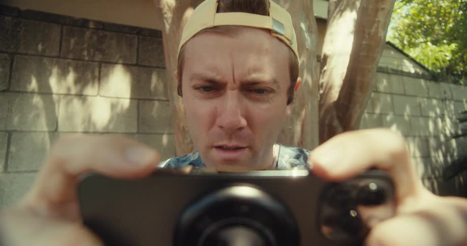 A man intensely focuses on taking a photo or video with a largelens smartphone camera outdoors