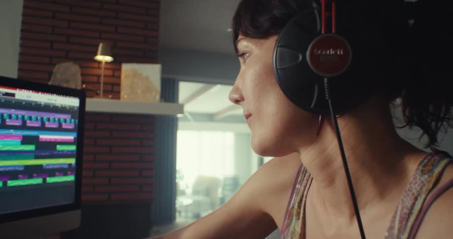 Woman sitting at a computer in her living room listens to music on her headphone