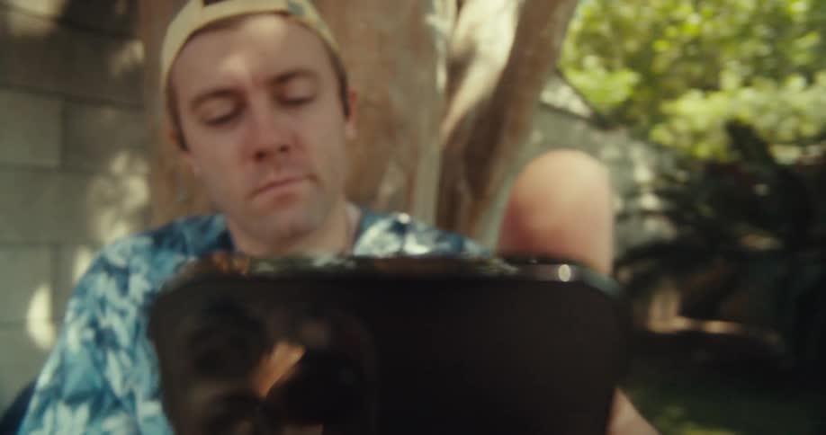 Man puts his phone close to the ear while sitting under a backyard tree at daytime