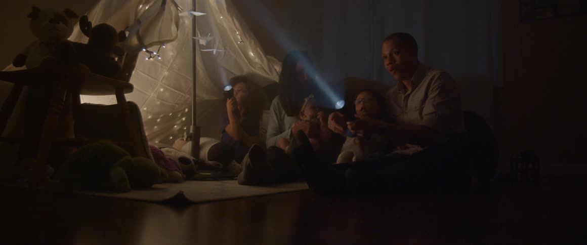 A family uses flashlights while playing in an indoor fort