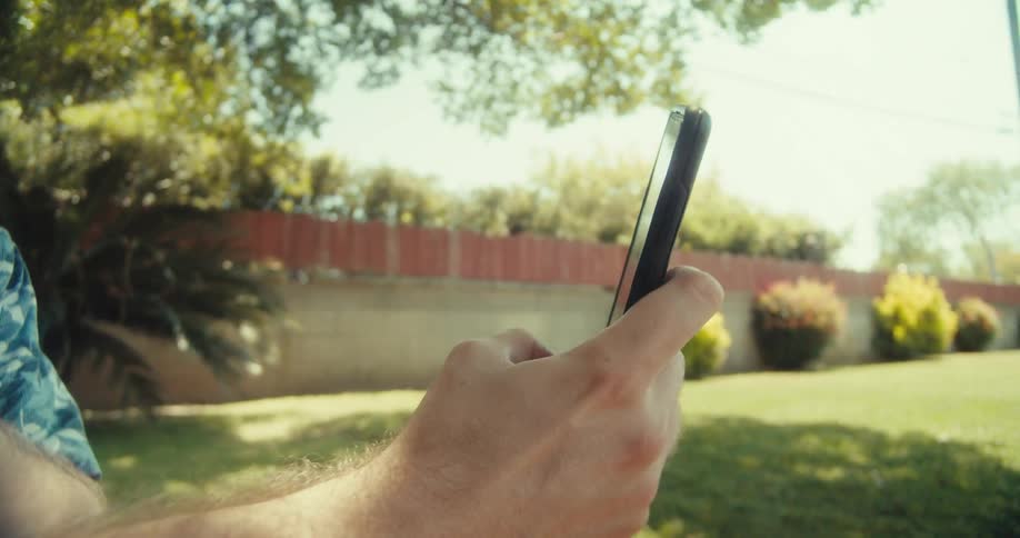 Man in a floral button up taking a selfie under a tree in the backyard