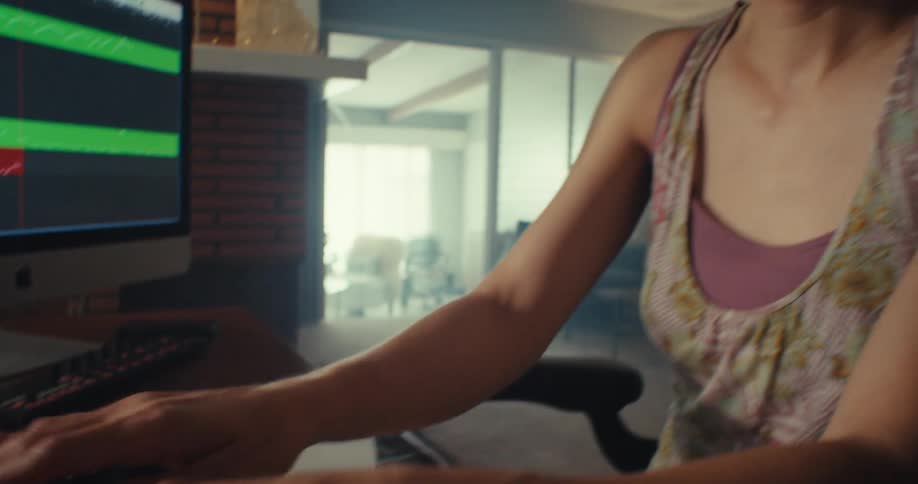 A woman in a room playing music on a keyboard and listening through headphones