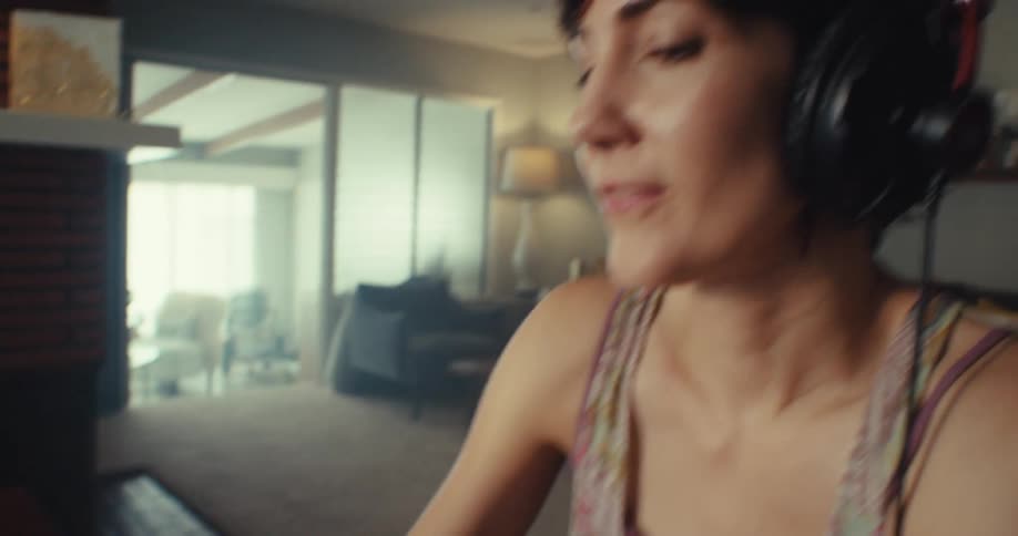 Woman uses a midi keyboard controller while sitting at home during the daytime