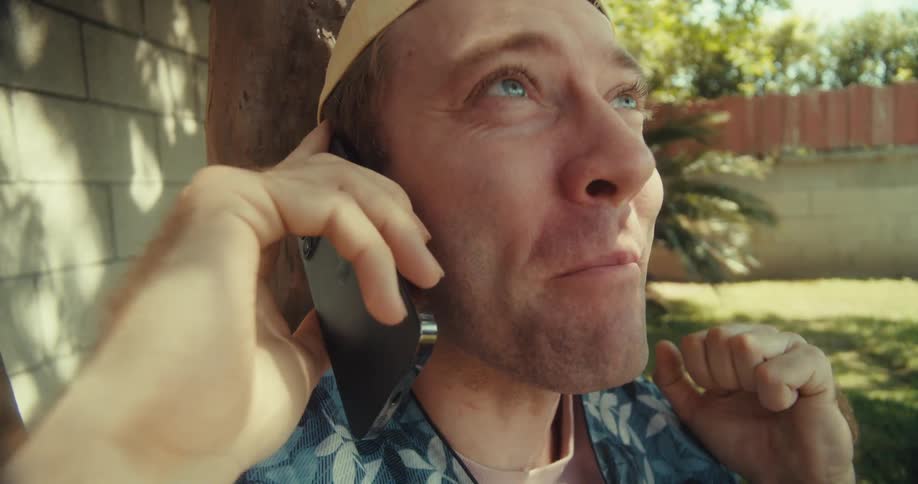 A man seated under the tree shouts while on a call at daytime