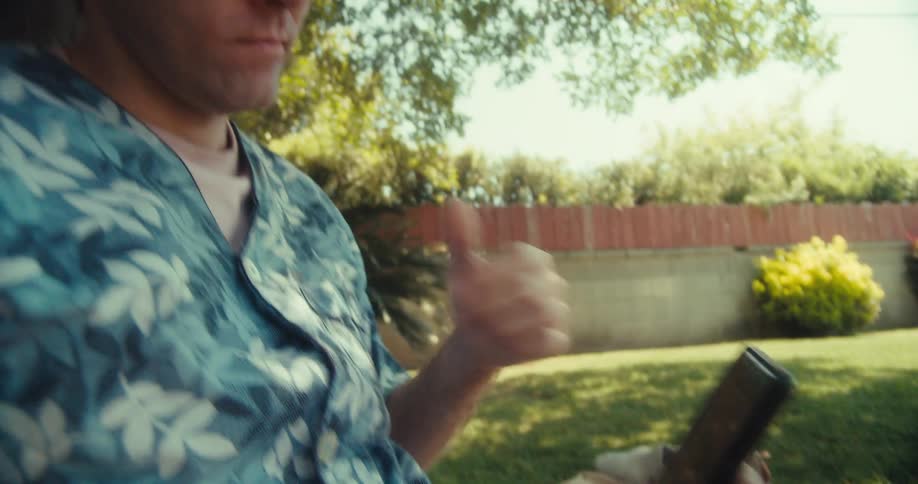 A man sits by a tree in the yard while using a cell phone