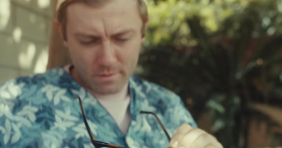 A man cleans his glasses with his shirt
