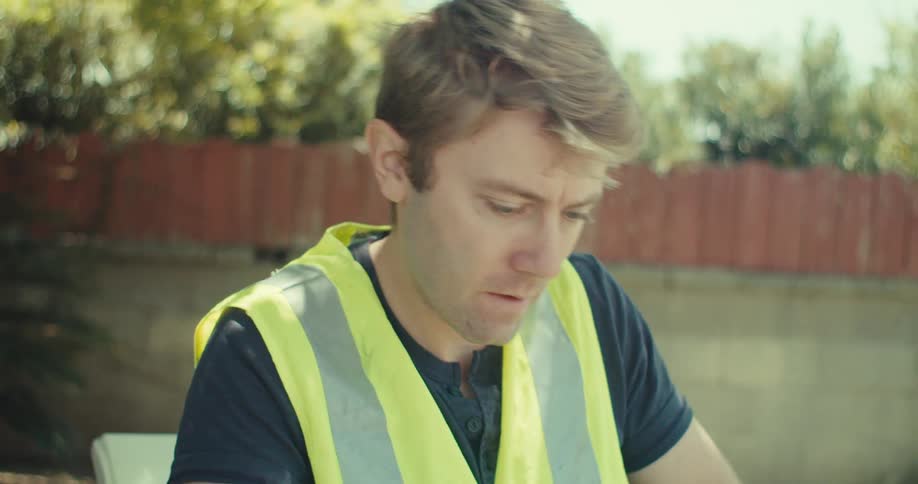 Man writes a sticky note and attaches it to a blueprint while at a table in the yard on a summer day