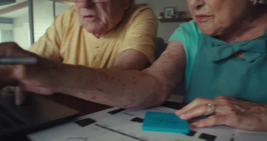An elderly couple sits at a laptop while the woman points something out on the screen