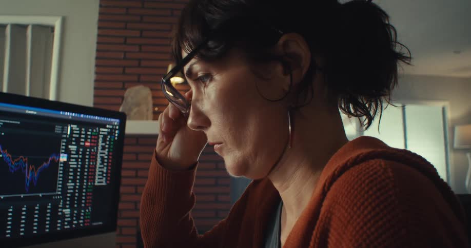 A woman indoors is focused on checking stock data on her computer screen