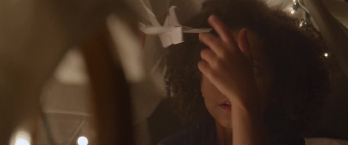 A little girl playing with paper cranes in a dark room