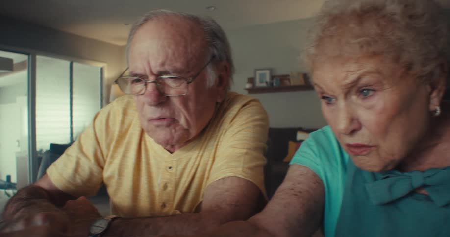 An elderly couple is looking at a laptop as they sit in their house