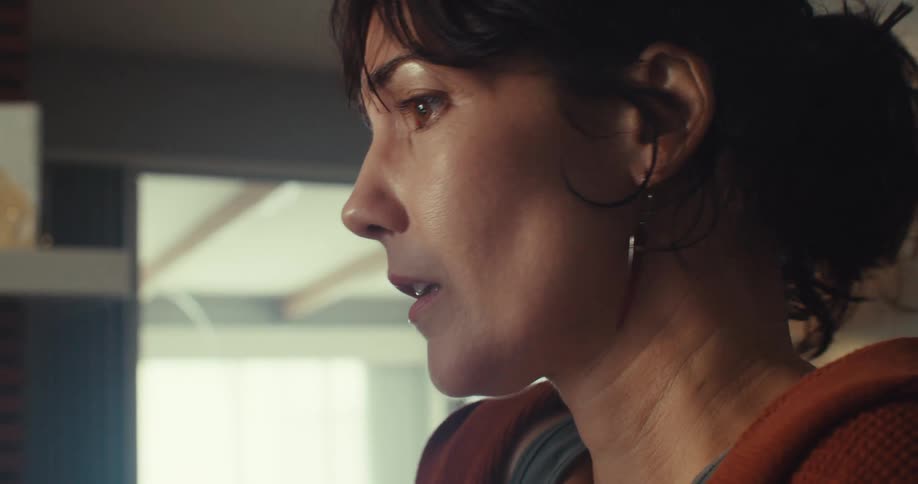 A closeup of a woman with dark hair pulled back looking intently with an expression of sadness and distress